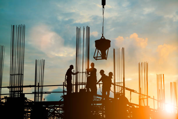 CIVIL ENGINEERING Silhouette of engineer and construction team working safely work load concrete on scaffolding on high rise building. over blurred background sunset pastel for industry background with Light fair